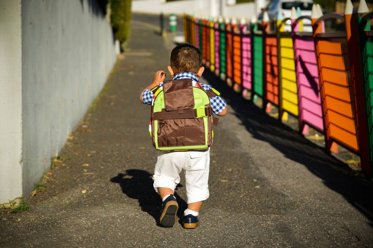 Enfant de dos portant un cartable sur un chemin bordé d’une clôture colorée