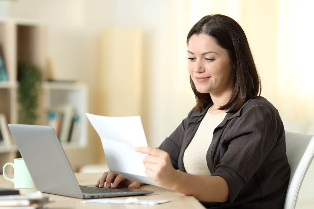 Une femme consulte un document devant son ordinateur.